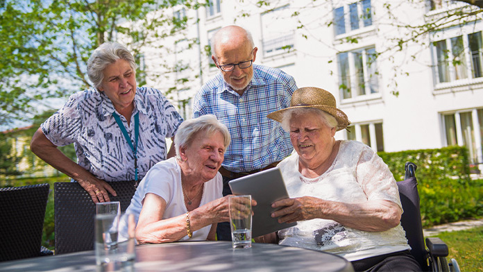 Im Garten blicken 2 stehende und 2 sitzende Senioren gemeinsam auf ein Tablet