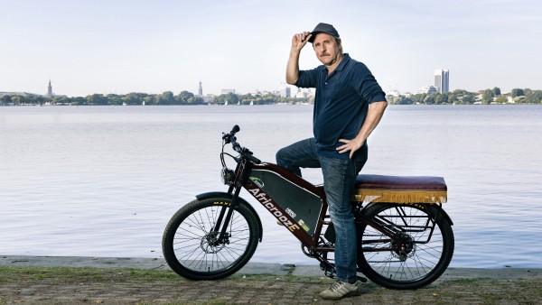 Actor Bjarne Mädel sits on the African E-Bike in front of the Alster