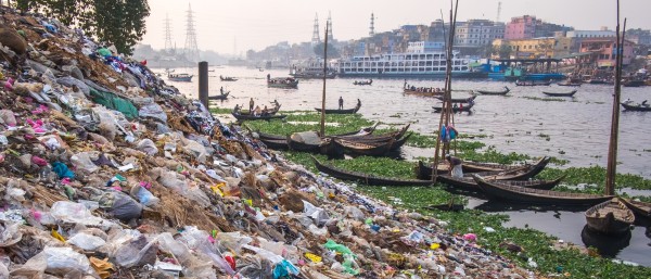 Müll und Plastikverschmutzung am Flussufer in Dhaka, Bangladesch, Flussufer und Boote im Hintergrund
