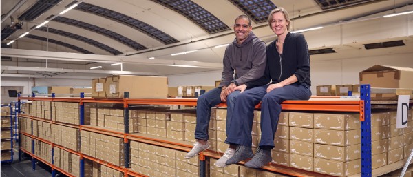 Wildling shoes founders Anna and Ran Yona sit on top of a shelf filled with shoe boxes.