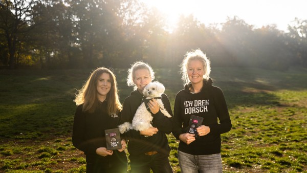 drei junge Frauen stehen auf einer Wiese mit einem Hund
