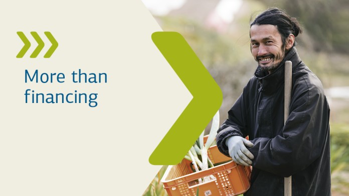 A man wearing safety clothing and a hard hat stands with his arms folded in front of a pile of rubbish