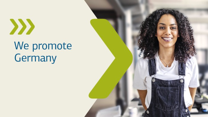 A man with a tablet in his hand stands in a production hall and smiles at the camera