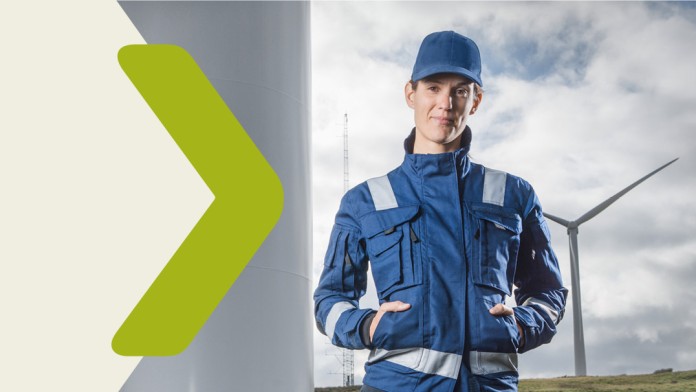 A woman stands in front of a wind turbine