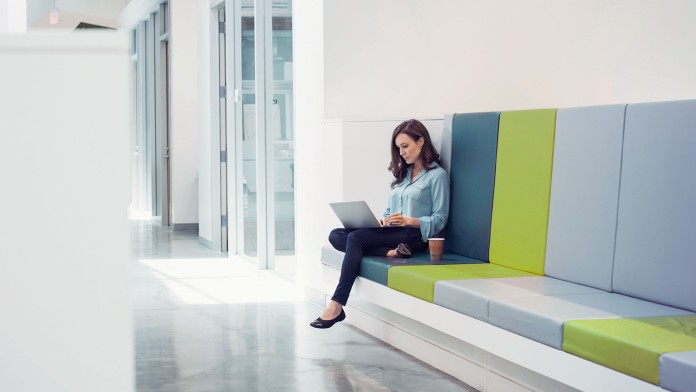 Junge Frau sitzt mit einem Laptop auf einer Sitzbank