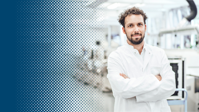 A scientist wearing a white coat stands in front of machines in a laboratory