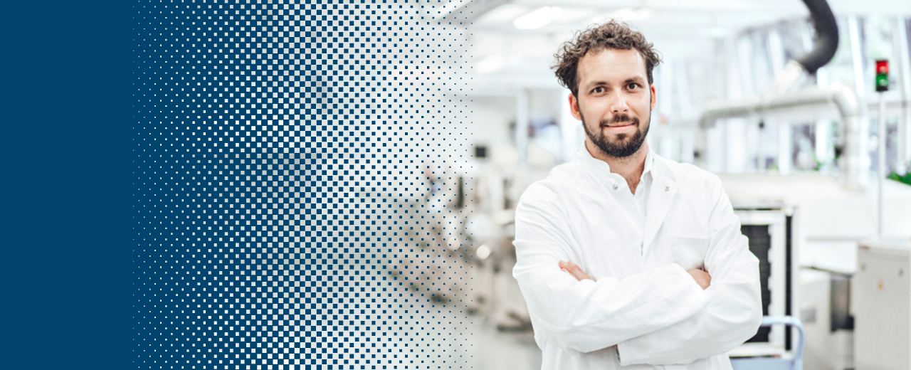 A scientist in a white coat stands in front of machines in a laboratory