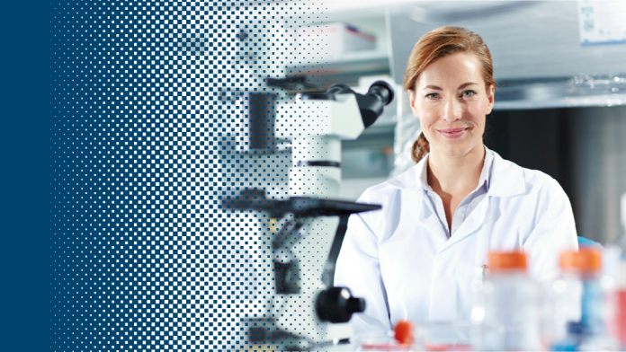 Frau mit einem weißen Kittel im Forschungslabor vor einem Mikroskop