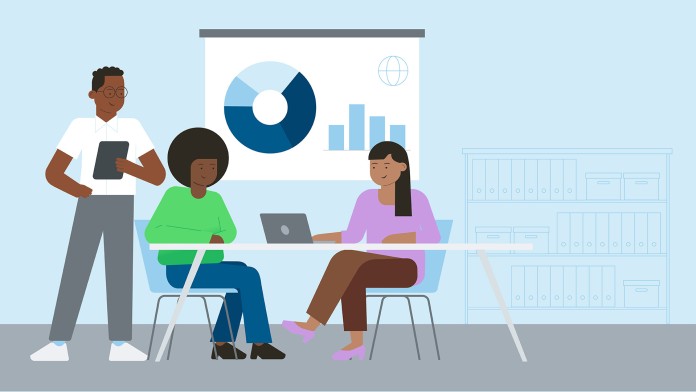 Three people in an office, sitting at a laptop and in front of a presentation chart.