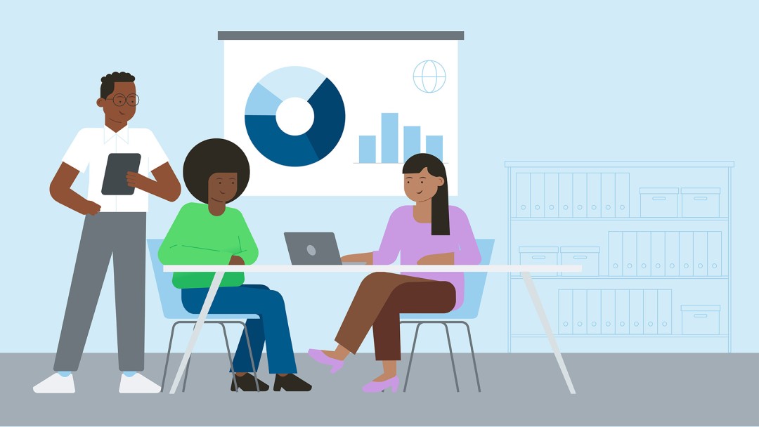 Three people in an office, sitting at a laptop and in front of a presentation chart.