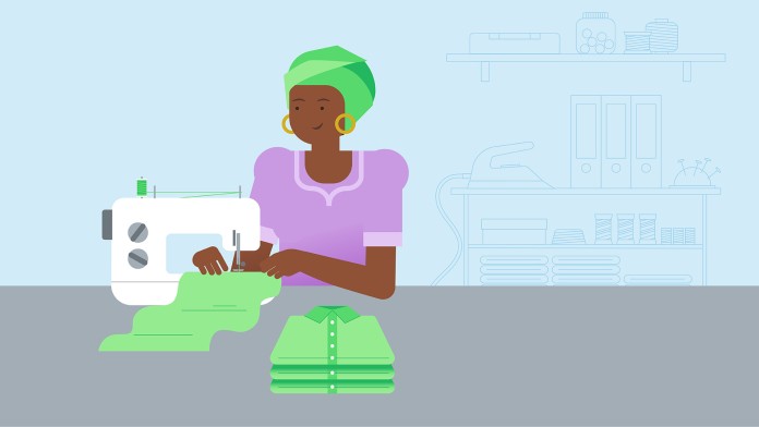 A seamstress sits at a sewing machine. A cupboard with folders can be seen in the background.