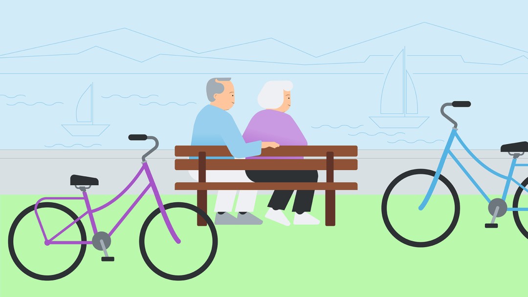 Two senior citizens are sitting on a bench overlooking a river. Their bicycles are parked next to them.
