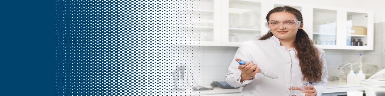 A woman in a white coat and protective goggles stands in a laboratory