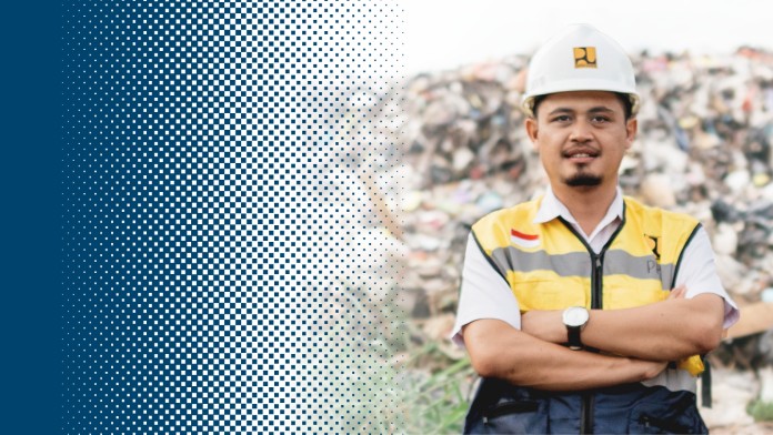 A man wearing safety clothing and a hard hat stands with his arms folded in front of a pile of rubbish