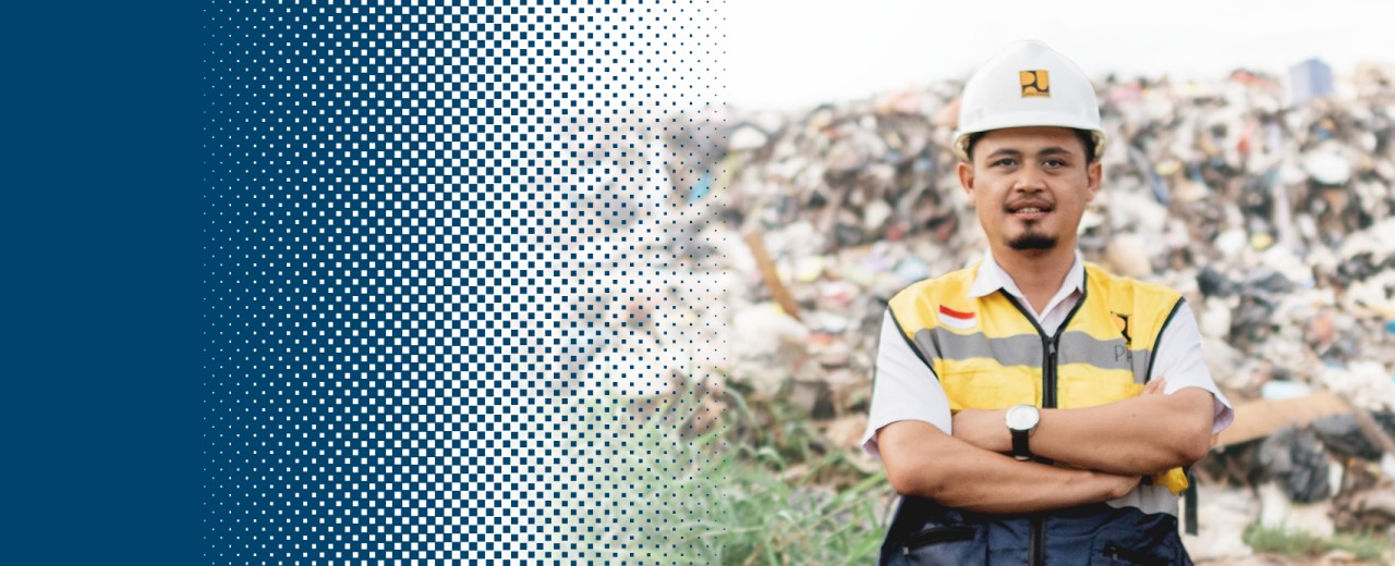 A man wearing safety clothing and a hard hat stands with his arms folded in front of a pile of rubbish