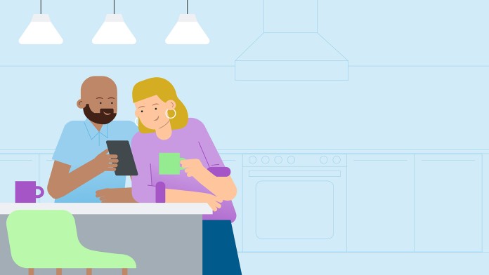 Two people are standing in the kitchen looking at their mobile phones