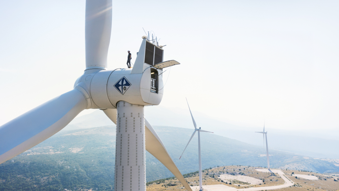 Ein Landschaftsfoto mit Windrädern, auf dem vordersten ein Handwerker im Fokus