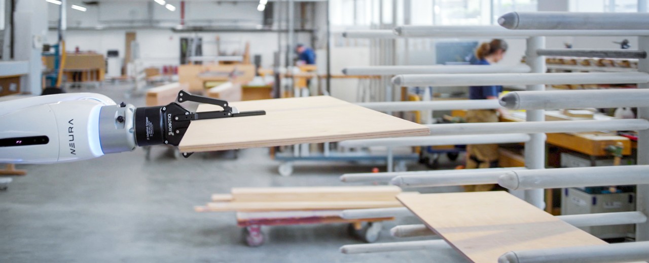 Ein Industrieroboter greift eine Holzplatte in einem Setting moderner Fertigung. Zum Audrcuk kommen hier Automatisierung und Industrie 4.0 in der Produktion.