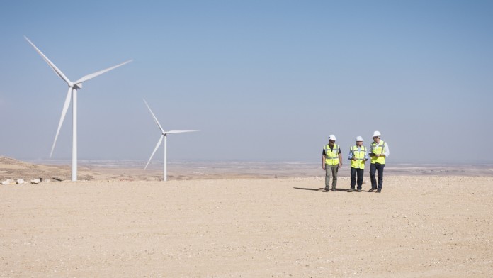 Windkraftanlage in Wüstenlandschaft mit Technikern. Themen sind erneuerbare Energien, nachhaltige Energieerzeugung und Energiewende.