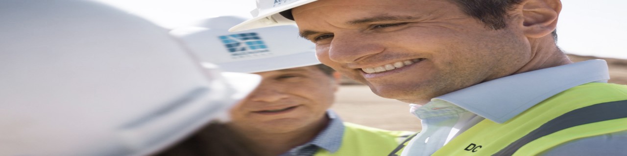 Ingenieure mit Schutzhelmen und Warnwesten besprechen ein Bauprojekt. Inhaltlich sind hier die Themen Infrastruktur, Planung und Zusammenarbeit gleichermaßen abgebildet.
