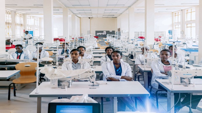 Zahlreiche Auszubildende sitzen in einer Textilwerkstatt an Nähmaschinen. Themen sind berufliche Bildung, Beschäftigung und nachhaltige Entwicklung in Afrika.