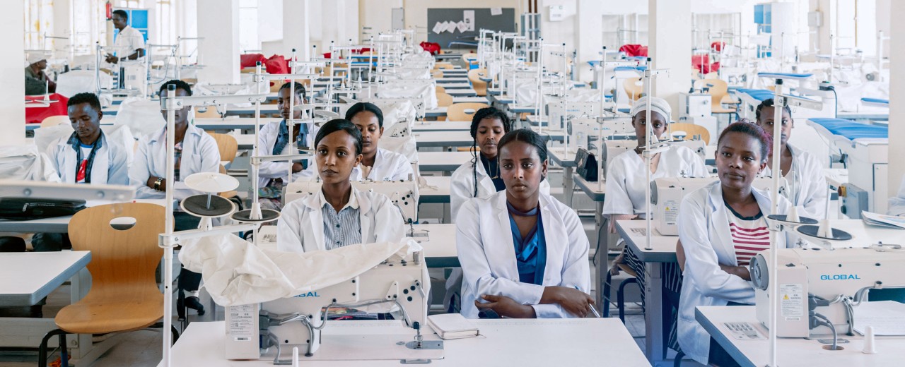 Zahlreiche Auszubildende sitzen in einer Textilwerkstatt an Nähmaschinen. Themen sind berufliche Bildung, Beschäftigung und nachhaltige Entwicklung in Afrika.