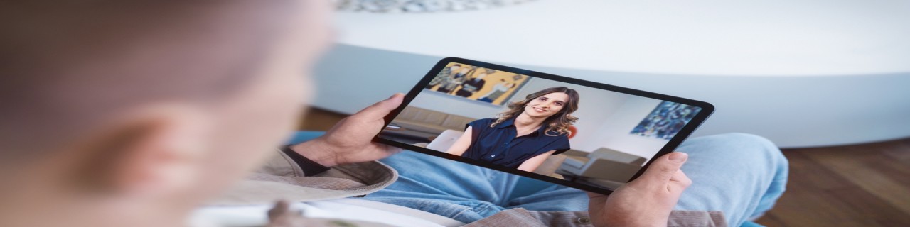 Eine Person hält ein Tablet in den Händen, auf dem eine Frau zusehen ist.