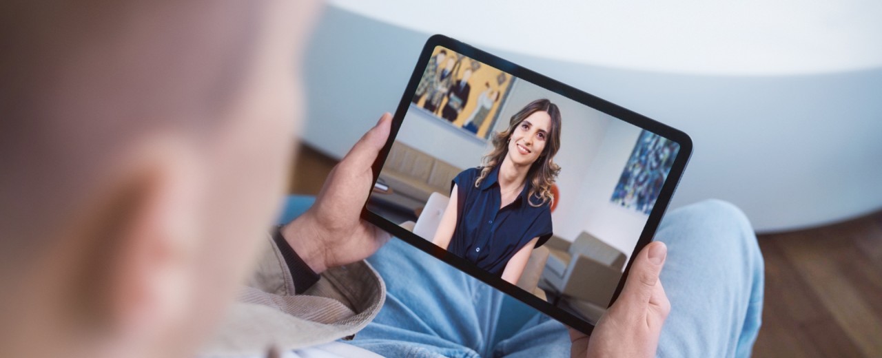 Eine Person hält ein Tablet in den Händen, auf dem eine Frau zusehen ist.