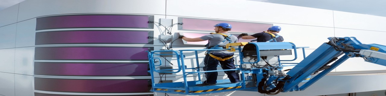 Techniker installieren Solarmodule an einer Gebäudefassade. Hier kommen die Themen erneuerbare Energien, Photovoltaik und nachhaltige Energieversorgung zum Ausdruck.