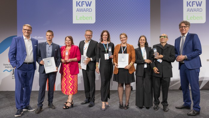 Preisverleihung des KfW Award Leben in der Kategorie „Inklusion leben- Behindertensport vereint Kommunen“. Gruppenfoto der Preisträger auf der Bühne.