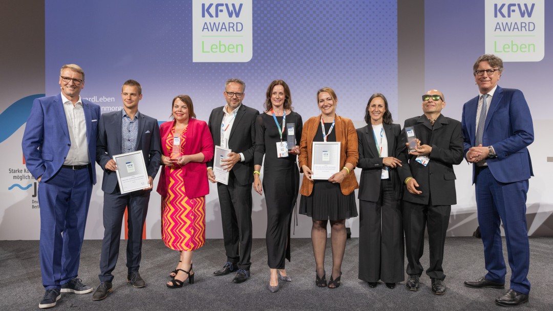 Preisverleihung des KfW Award Leben in der Kategorie „Inklusion leben- Behindertensport vereint Kommunen“. Gruppenfoto der Preisträger auf der Bühne.