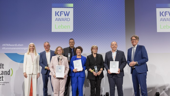 Preisverleihung des KfW Award Leben in der Kategorie „Bezahlbares und flächeneffizientes Wohnen“. Gruppenfoto der Gewinner auf der Bühne.