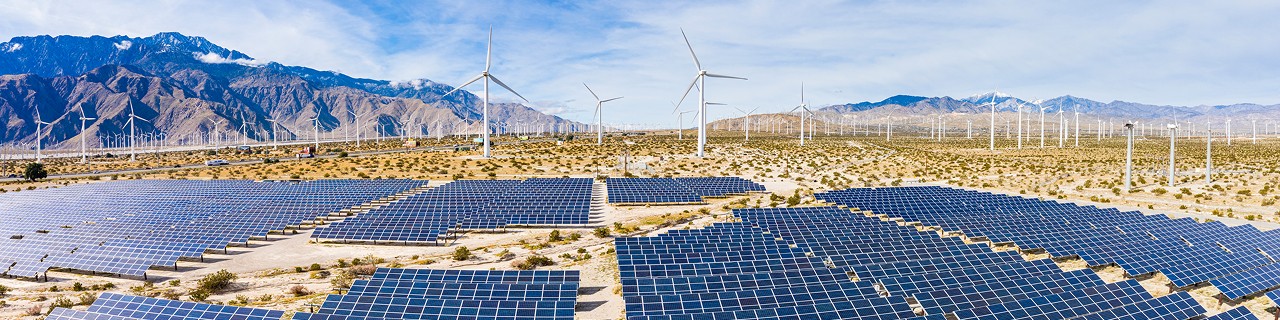 Solarpark vor Windpark mit Bergen im Hintergrund 