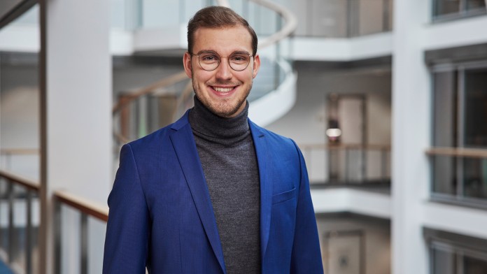 Portraitaufnahme von Hendrik Huwe in der Ostarkade in Frankfurt, er trägt eine Brille, einen dunkelgrauen Rollkragenpullover und blaues Sakko