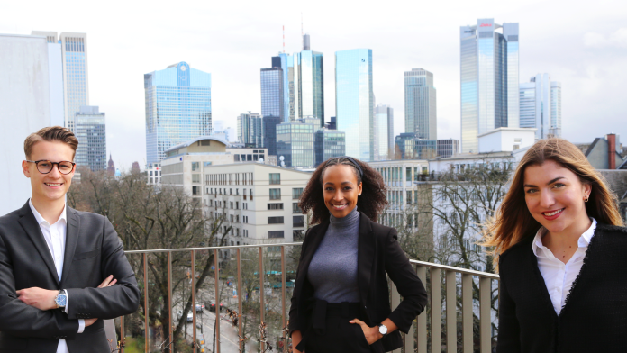 Drei Studierende befinden sich auf der Dachterasse der KfW. Hinter ihnen ist die Skyline von Frankfurt zu sehen