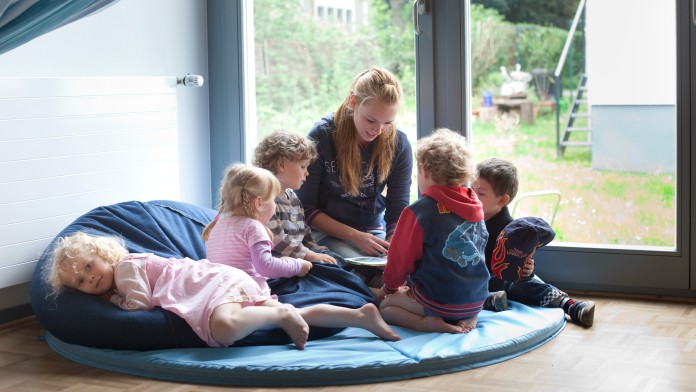 fünf Kinder sitzen um eine Erzieherin herum und hören ihr beim Vorlesen zu