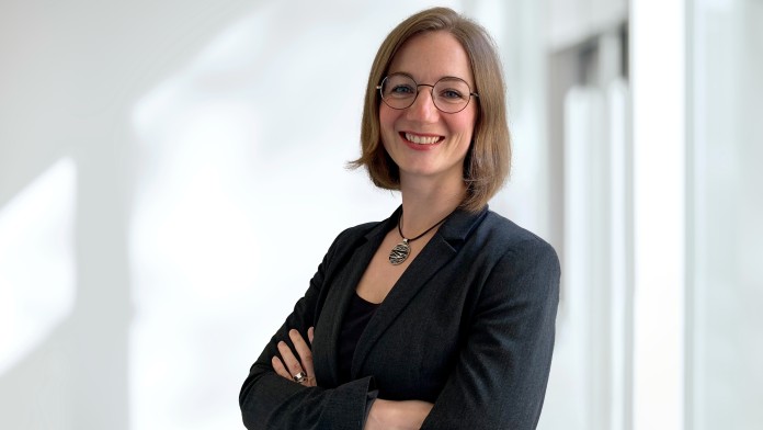 Elisa Cuadra, Mitarbeiterin des Indocenters der KfW, sie trägt einen schwarzen Blazer und steht mit gekreuzten Armen in einem Foyer.