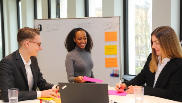 Drei Stuzubis besprechen in einem agilen Arbeitsumfeld ihre nächsten Projektschritte. 