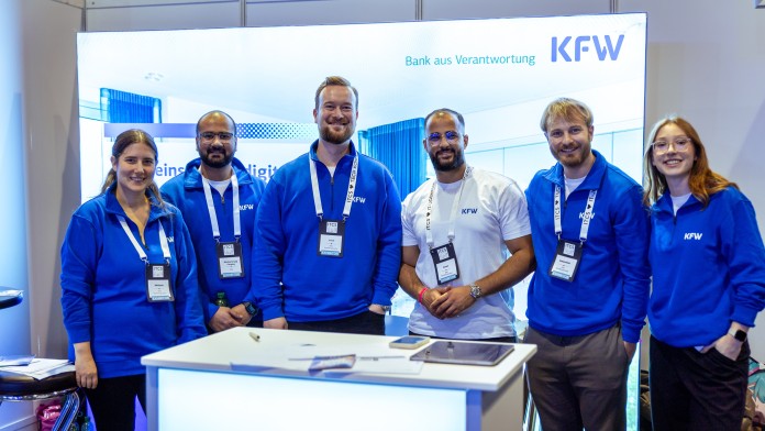 Aufnahme von Kollegen und Kolleginnem auf einer IT-Messe. Die Personen tragen blaue KfW Sweater, ein Kollege trägt ein weißes T-Shirt und sie lächeln freundlich in die Kamera.