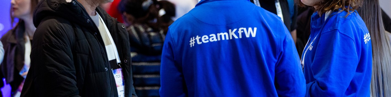 Entfernte Aufnahme einer Gesprächssituation auf der ITCS-Messe. Man sieht die Rückseite der blauen KfW Sweater auf der #TeamKfW steht.