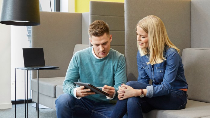 Zwei Trainees, eine Frau und ein Mann sind Casual Business in Blue Jeans mit Hemd und Pullover gekleidet, halten ein Tablet in der Hand und sprechen über einen Arbeitscase