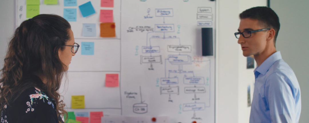 Zwei Personen arbeiten an einem Whiteboard und besprechen einen IT-Case, dessen Prozess darauf abgebildet ist