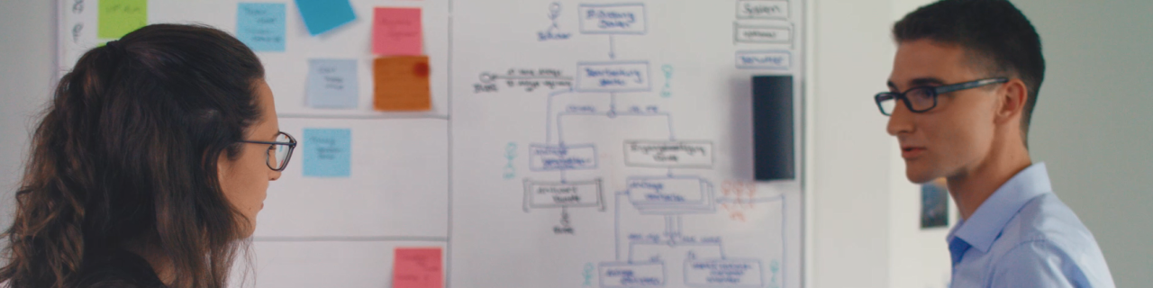 Zwei Personen arbeiten an einem Whiteboard und besprechen einen IT-Case, dessen Prozess darauf abgebildet ist