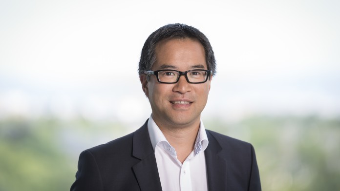 Ein Portraitfoto von Dr. Christian Chua, aus der Konzernkommunikation. Er trägt einen schwarzen Anzug und ein weißes Hemd ohne Krawatte. 