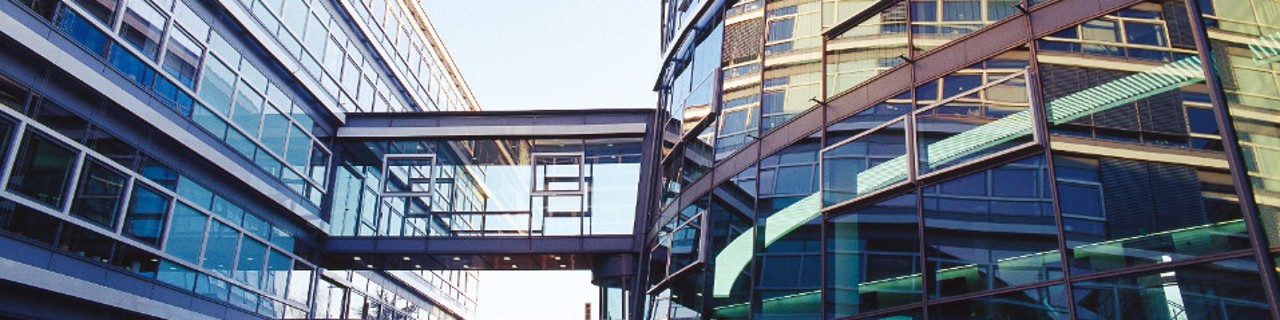 Außenansicht der KfW-Niederlassung in Bonn mit zwei modernen Glasgebäuden, verbunden durch einen verglasten Übergang bei blauem Himmel. 