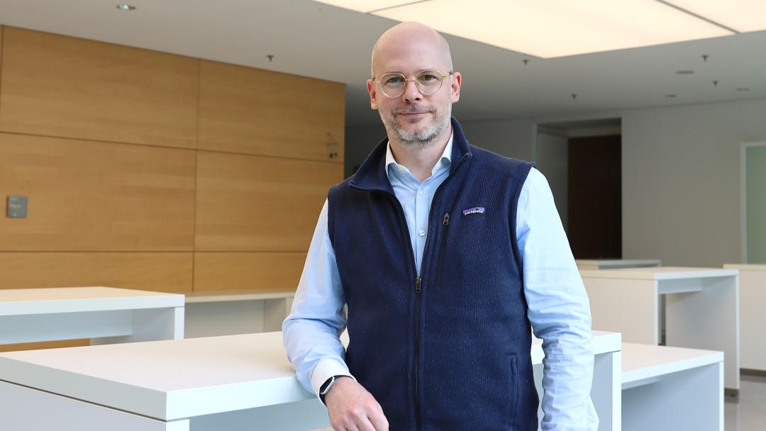 Portraitbild von Torsten Schildwächter, Mitarbeiter der Internen Revision der KfW, er trägt eine Brille sowie hellblaues Hemd mit dunkelblauer Weste und steht in einem Foyer der KfW.