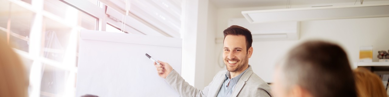 Ein Mann steht vor einem Flipchart und präsentiert vor einer Gruppe