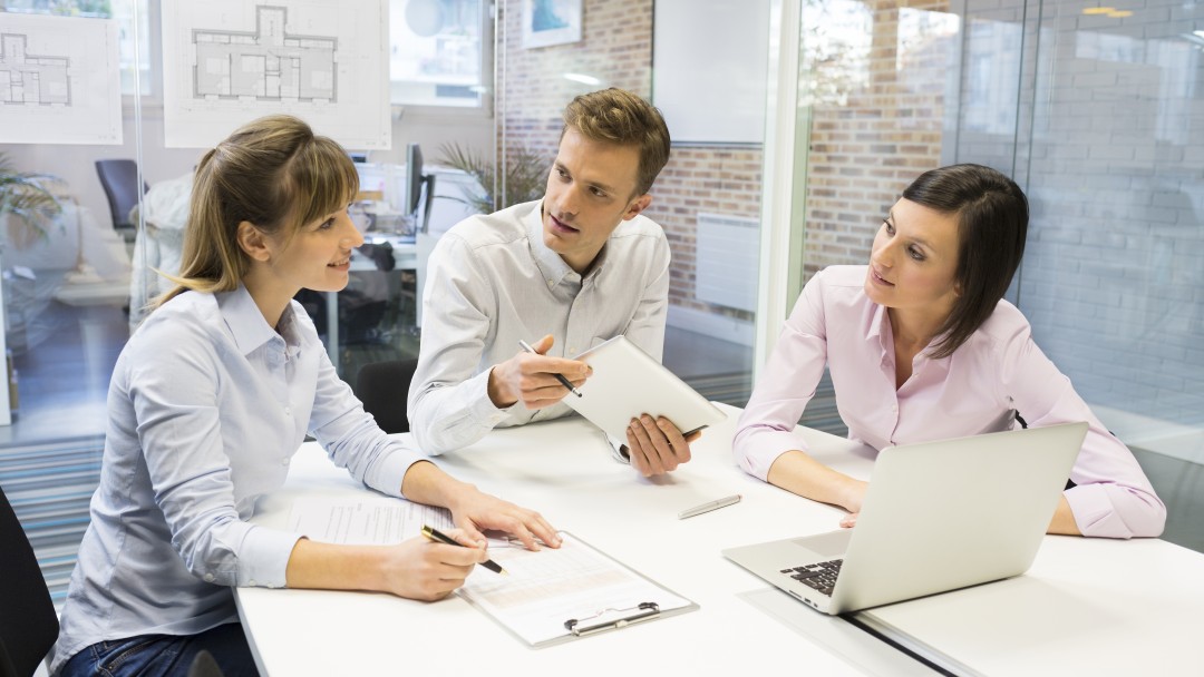 Drei Personen sitzt zusammen an einem Tisch und diskutieren Arbeitsergebnisse