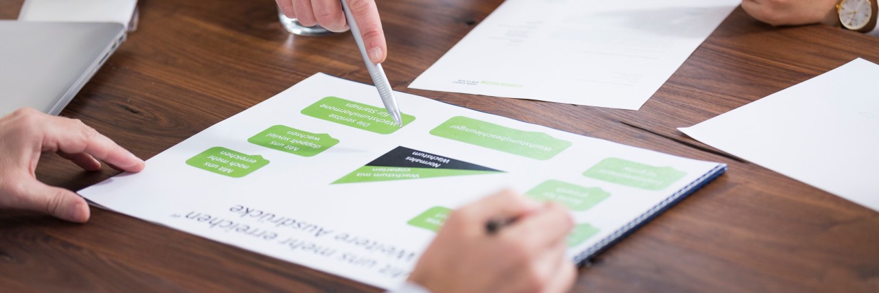There are documents on a meeting table, and you can also see the hands and arms of people working with the documents