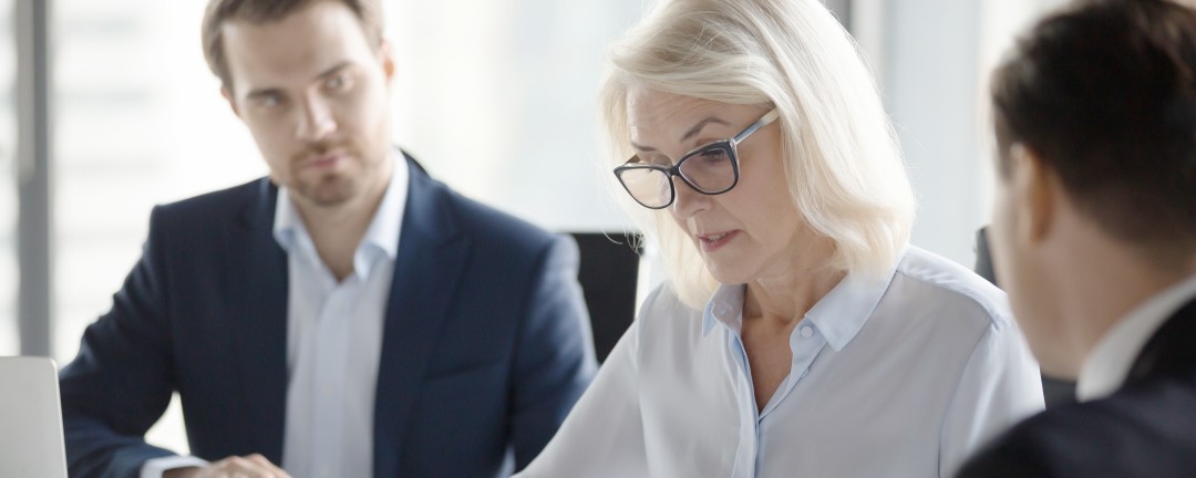 Besprechungssituation mit einer Frau, die auf ein Dokument schaut, zwei Männer schauen sie an